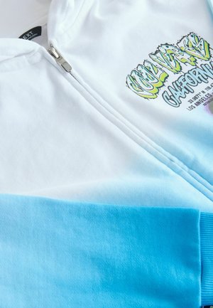 Felpa con zip di colore bianco e tessuto blu sfumato. Presenta una grafica stampata con testo in verde e viola, e polsini a coste.
