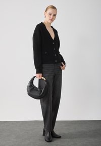 Melna adīta kardigāna ar dziļu V veida kakla izgriezumu un pogām, kombinēta ar augsto vidukli tumši pelēkajām džinsām. Tur rokās melna ādas soma ar koka rokturi.