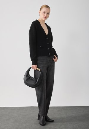 Crna pletena kardigan s dubokim V-izrezom i gumbima, uparen s tamnosivim trapericama visokog struka. Drži crnu kožnu torbu s drvenom drškom.