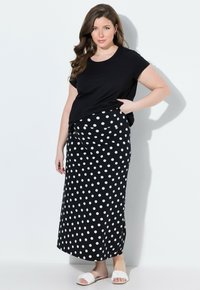 Zwarte t-shirt en een lange, zwarte rok met grote witte stippen. De outfit heeft een comfortabele pasvorm en zachte stof. Platte witte sandalen.