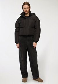 Czarna kurtka puchowa o skróconym fasonie, z dużymi wypełnieniami i kapturem. W połączeniu z luźnymi czarnymi dżinsami i brązowymi butami slip-on.