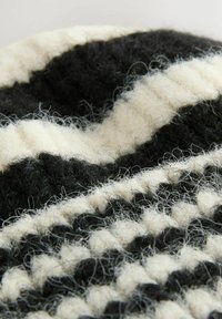 Gestructureerde wollen stof met een patroon van afwisselend zwarte en witte strepen, die verschillende diktes en donzige vezels tonen.