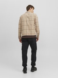 Beige checkered shirt jacket with a collar, button cuffs, and a straight cut. Black cargo pants with side pockets and elastic cuffs.