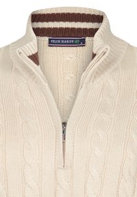 Kermanvärinen palmikkoneulepaita, jossa puolivetoketjullinen kaulus. Ruskea- ja valkoraidallinen resorikaulus lisää tekstuuria. Sisäpuolella on brändätty merkki.