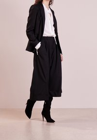 Black tailored blazer over a white blouse with button details, paired with loose black culottes and black heeled boots with zippers.