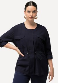 Granatowa tunika wykonana z lekkiego materiału, z okrągłym dekoltem, dwiema kieszeniami na piersi oraz regulowanymi sznurkami w talii.