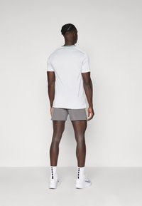 White athletic shirt with green accents, gray shorts, and white sneakers. The shirt features a round neck and short sleeves.