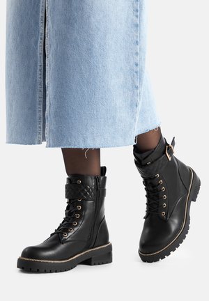 Schwarze Leder-Schnürstiefeletten mit seitlichen Reißverschlüssen und gesteppte Riemendetails, getragen mit schwarzen Strumpfhosen und einem hellblauen Jeansrock.