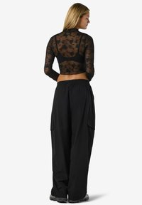 Fekete, hosszú ujjú hálós felső virágmintával, laza fekete cargo nadrággal párosítva, oldal zsebekkel és rugalmas derékkal.
