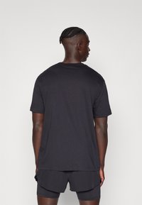 Schwarzes T-Shirt mit kurzen Ärmeln, runder Ausschnitt, lockere Passform, glatte Textur, getragen mit passenden dunklen Shorts, schlichtes Design.