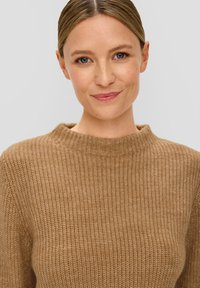Brauner gerippter Strickpullover mit hohem Kragen, der eine weiche Textur und einen lockeren Schnitt aufweist, präsentiert vor einem neutralen Hintergrund.