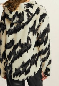 Blød, struktureret fleece-sweatshirt i creme med sort abstrakt mønster. Har hætte med snøre og buet kant samt lange ærmer.