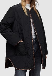 Czarna pikowana kurtka z okrągłym kołnierzem, zatrzaskami i lamówką w panterkę wzdłuż krawędzi i kieszeni. Widoczna przednia kieszeń.
