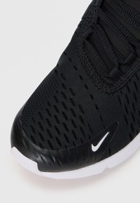 Črne športne čevlje z mrežastim zgornjim delom, ki ima prezračevalne luknje, teksturiran sintetičen zaščitni del na prstih in bel Nike logotip na strani.