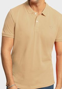 Polo de color beige hecho de una tela suave, con un cuello clásico, una tapeta de tres botones y un sutil logo bordado en el pecho.