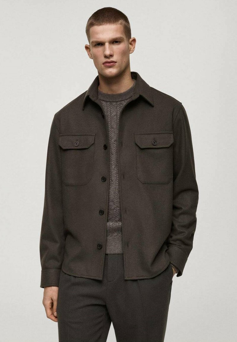 Dark brown shirt jacket made of soft fabric, featuring two chest pockets, a button front closure, and a classic collar. Worn over a textured sweater.