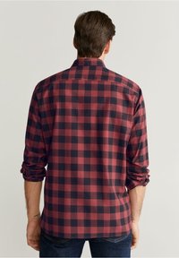 Chemise à manches longues à carreaux rouges et bleu marine, avec un col boutonné, des poignets retroussés et un ourlet droit. Tissu en coton avec une texture lisse.