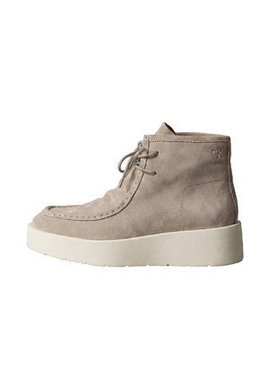 Beiger Wildleder-Stiefel mit Schnürung vorne, dicker weißer Sohle und kleinem geprägtem "ck" Logo nahe der oberen Ferse.