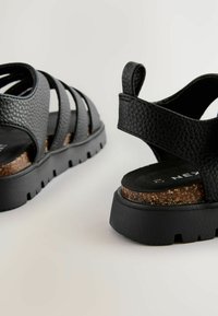 Schwarze Textur-Sandalen mit mehreren Riemen, einer gepolsterten Kork-Zwischensohle und einer robusten Gummi-Außensohle mit einem profilierten Design für besseren Halt.