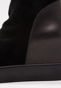 Botín negro hasta el tobillo que combina ante y cuero suave, con punta redonda y un diseño elegante y minimalista.