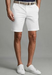 Valkoiset puuvillashortsit, joissa on sivutaskut, kudottu beige vyö ja valkoiset sneakerit. Silkkinen rakenne ja mukautettu istuvuus, sopii rentoon käyttöön.