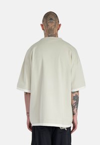 Prehrnuté krémové tričko vo veľkosti oversized, vyrobené z mäkkej bavlny. Má krátke rukávy, okrúhly výstrih a jemné biele lemovanie na rukávoch.