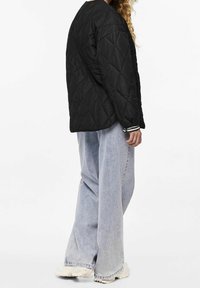 Black quilted jacket with a round neckline, featuring a textured pattern, paired with light blue wide-leg jeans and chunky white sneakers.