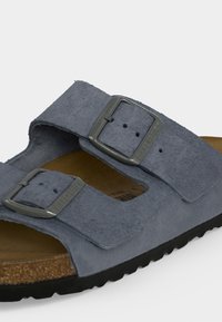 Blå mockasinsandal med två justerbara metallspännen och en formad korkfotbädd på en svart gummisula.