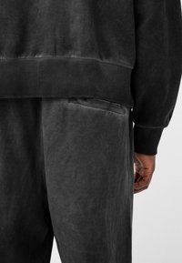 Sudadera con capucha y pantalones deportivos en gris oscuro con textura suave y lisa. Puños y cintura acanalados. Detalle sutil de bolsillo en los pantalones. Diseño minimalista.