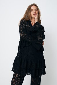 Rochie neagră din dantelă cu mâneci lungi, volane în straturi și model floral. Textură ușoară, combinată cu colanți din dantelă asortați.