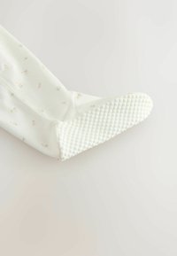 Biała skarpetka z różowym kwiatowym wzorem, posiadająca teksturowaną, kropkowaną podeszwę zapewniającą przyczepność i wygodę. Miękka tkanina, gładka faktura, długość do kostki.