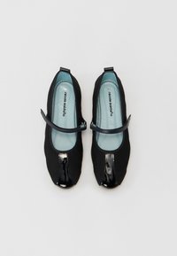 Sapatilhas de balé pretas com um cabedal em tecido e bico brilhante em verniz. Apresentam uma tira estilo mary jane e uma palmilha azul-clara, texturizada com pequenas perfurações.