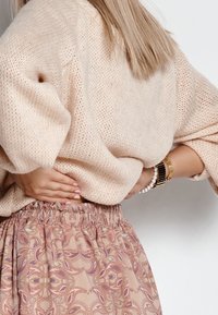 Beige stickad tröja med löst sittande passform och mjukt material. Rosa mönstrad kjol med elastisk midja, som har intrikata, snurrande mönster.
