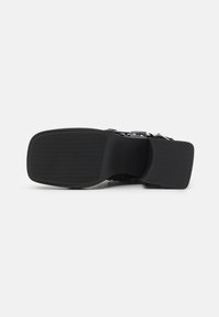 Black sandal sole with a textured surface, flat design, and a wider heel for stability. Features a smooth, rubbery finish and minimal profile.