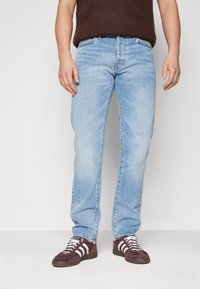 Jeans din denim albastru deschis cu un croi drept, design cu cinci buzunare, decolorare subtilă și detalii din metal. Asociați cu adidași maron închis.