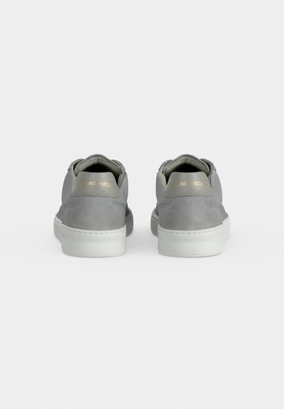 Ζευγάρι χαμηλά γκρι σουέντ sneakers με λευκές σόλες, ορατά από πίσω σε απλό ανοιχτό φόντο.