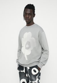 Sudadera gris con un gran gráfico floral blanco. El modelo lleva pantalones estampados en blanco y negro con un diseño floral similar.