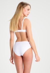 Hvit bh og høyinnsittende truser laget av mykt stoff, med blonderdetaljer langs kantene. Glatt tekstur med justerbare stropper.