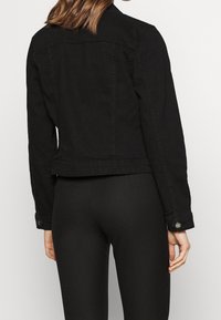 Musta farkkutakki, jossa on istuva muotoilu, napit ja kaksoisommellut saumat. Ominaisuuksia ovat lyhyt malli ja ei näkyviä logoja.