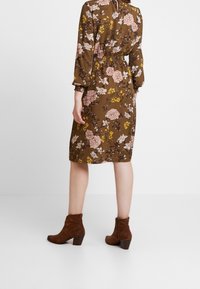 Braunes Blumenkleid mit langen Ärmeln, tailliertem Schnitt und knielangem Saum. Kombiniert mit braunen Wildleder-Stiefeletten.