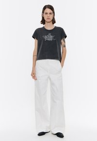 Camiseta gris corta con estampado gráfico, combinada con pantalones anchos blancos. Presenta mangas cortas y un corte relajado. Zapatos negros complementan el conjunto.