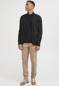 Lettvægts sort zip-up cardigan med ribbet krave, parret med en sort T-shirt, beige slim-fit bukser og grå sneakers.
