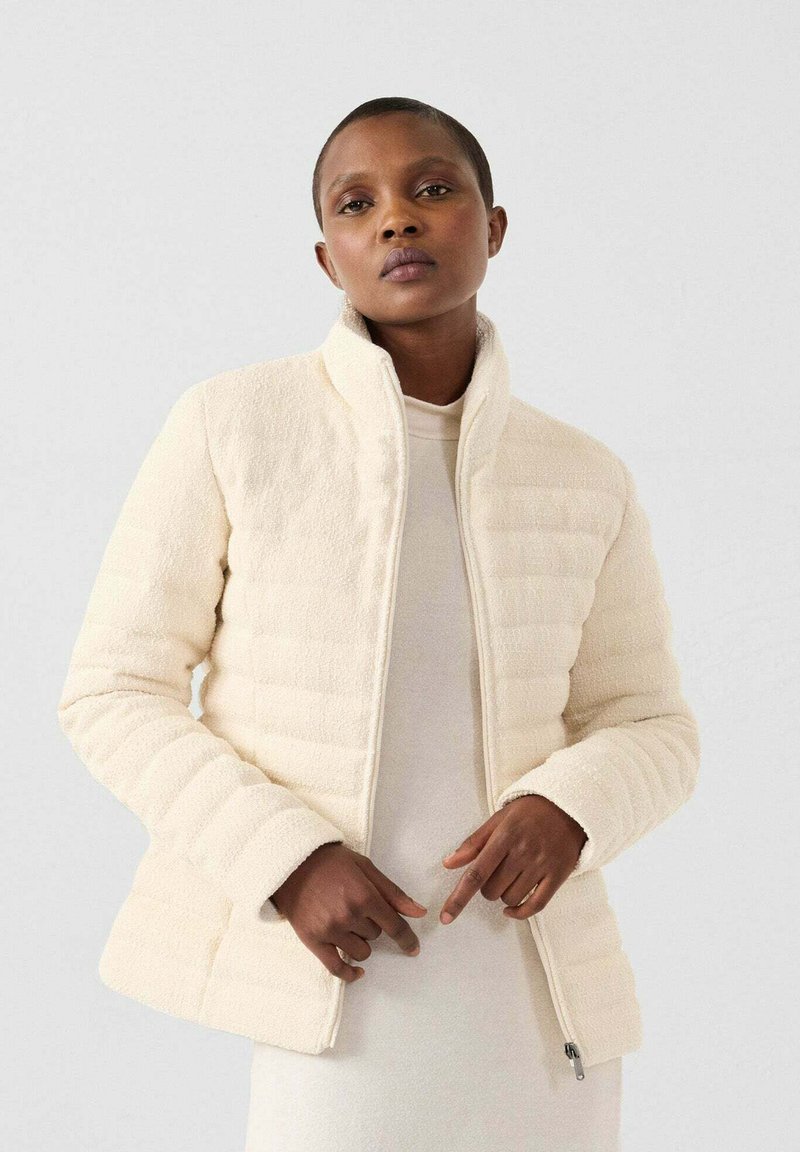 Chaqueta de crema clara con un diseño texturizado y acolchado. Cuello alto, cierre de cremallera y mangas ajustadas. Material suave con un acabado liso.