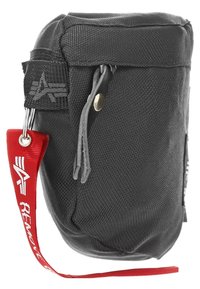 Svart tygpås med en strukturerad yta, dragkedjestängning och ett rött band med vit text. Inkluderar en nyckelring och en sidetikett.