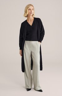 Czarny kardigan nałożony na czarny top z dekoltem w serek, zestawiony z jasnoszarymi, szerokimi spodniami w kratę oraz czarnymi, szpiczastymi butami.