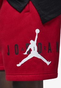 Shorts de algodón rojos con un gráfico de logo de Jordan en blanco y letras negras. Se puede ver tejido de malla negra en la cinturilla.