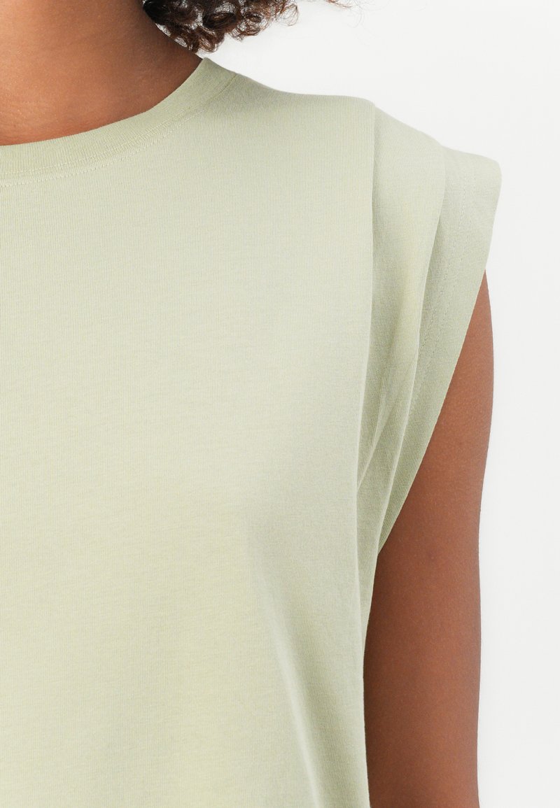 Helles grünes Kurzarmoberteil mit rundem Ausschnitt und leicht gepolsterten Schultern, aus weichem, strukturiertem Stoff.