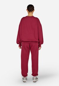 Bordový svetr a odpovídající tepláky z měkkého materiálu s volným střihem, obsahující žebrované manžety a pas.