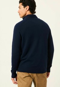 Navyblaues Strickpullover mit hohem Kragen, langen Ärmeln, gerippten Bündchen und Saum. Weiche Textur mit taillierter Passform.