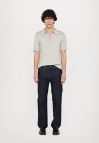 Polo grigio chiaro a maniche corte con colletto zip, abbinato a jeans a gamba dritta blu scuro e scarpe nere. Design semplice e pulito.